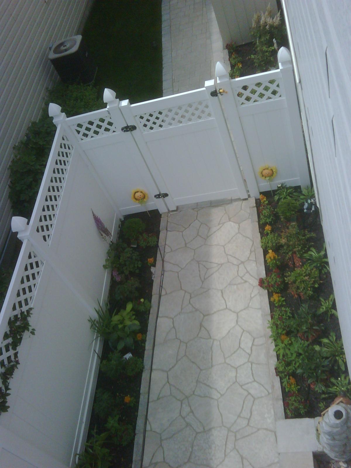 A stone-patterned path, planting borders and a side-yard gate.